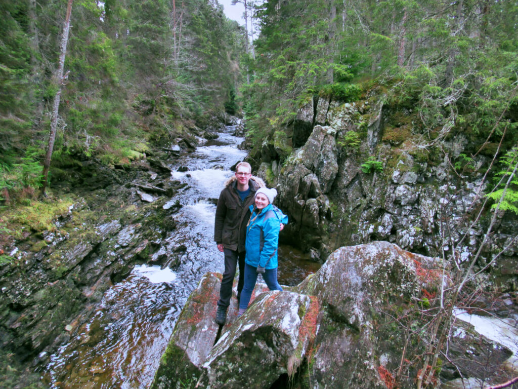 Zoe and boy-Zoe stood on a rock over looking a river, trees line either side of the river. 