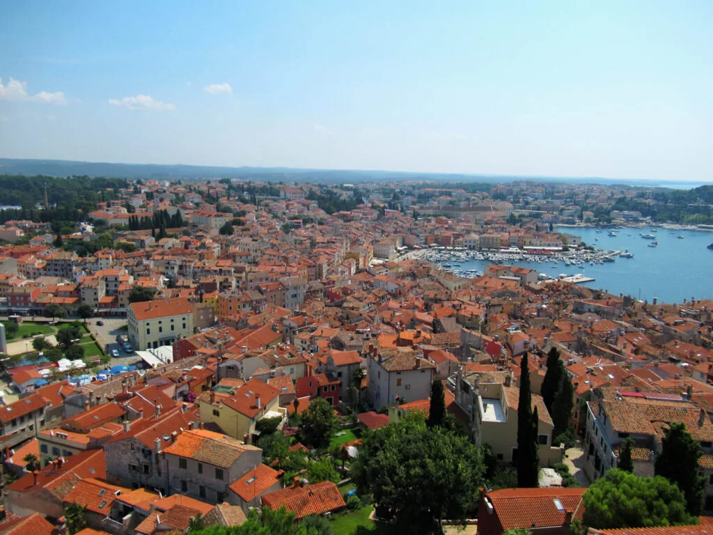 A birdseye view of Rovinj from the top of the bell tower. The orange roofs contrast with the blue sea and sky. Rovinj is worth visiting as a day trip from Pula to experience the feel of Venice and amazing Italian-influence food!
