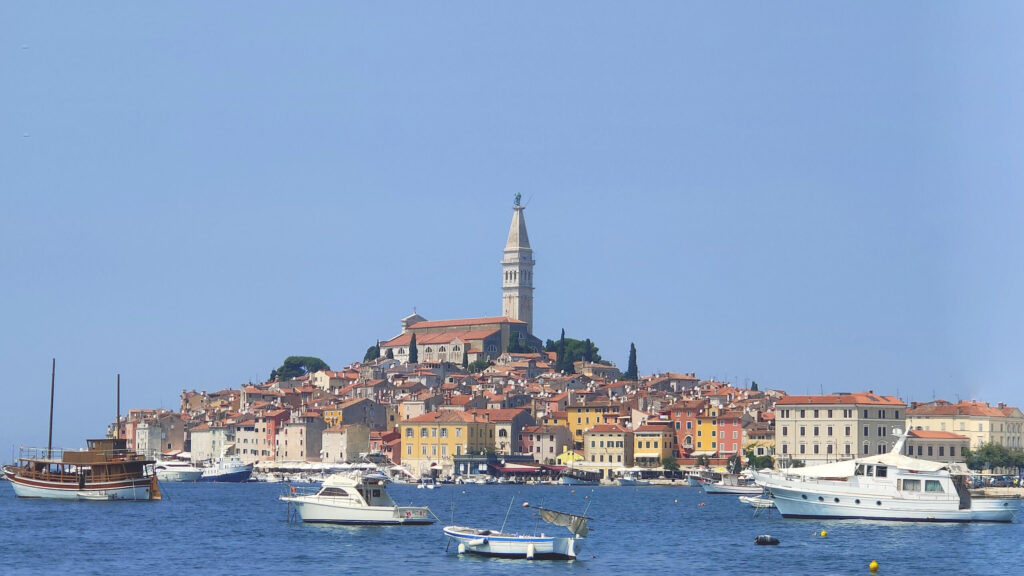The beautiful old town of Rovinj with brightly coloured buildings and the church and bell tower rising out the top. Boats in the marina are in the foreground. A great photo spot if you're visiting from Pula to Rovinj
