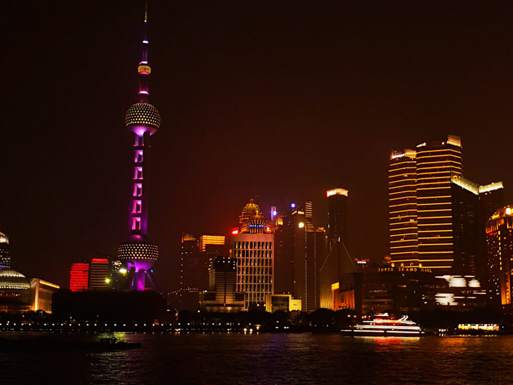 View of the Shanghai TV Tower from the Bund at night. The TV Tower is illuminated with pink and yellow lights against the dark of the night sky. A must see in a shanghai 3-day itinerary