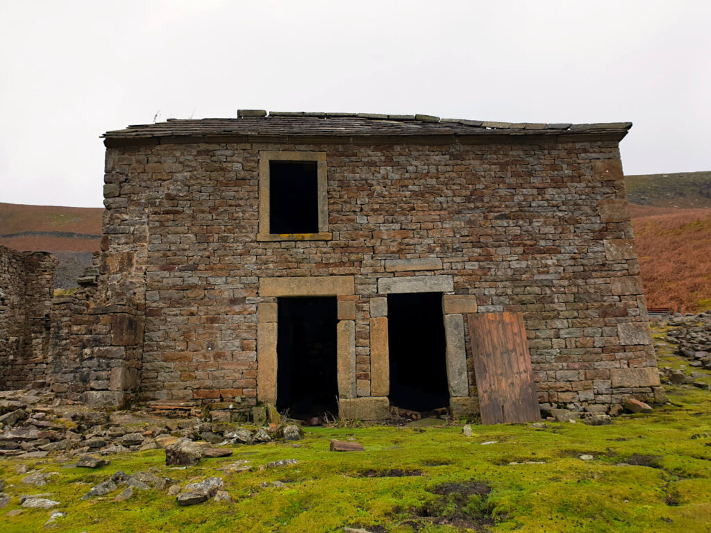 An abandoned farmhouse with two front doors and an upstairs window - very dark inside. The brickwork stands strong after years on the exposed Yorkshire Dales hillside - would you go inside?
