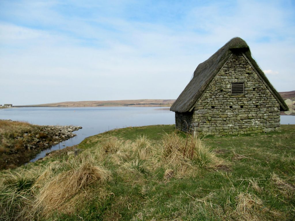 The restored medieval barn on the eastern shore of Grimwith Reservoir. The walking route takes you behind here and the holiday cottages