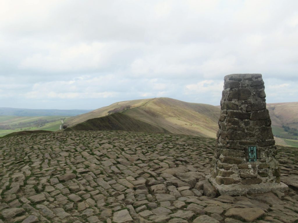 The stone trig point on the summit of Mam Tor with views looking west behind