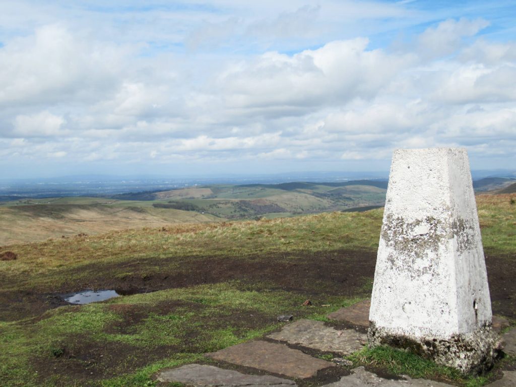 The trig point of Shining Tor with impressive views behind over the last few Peak District hills