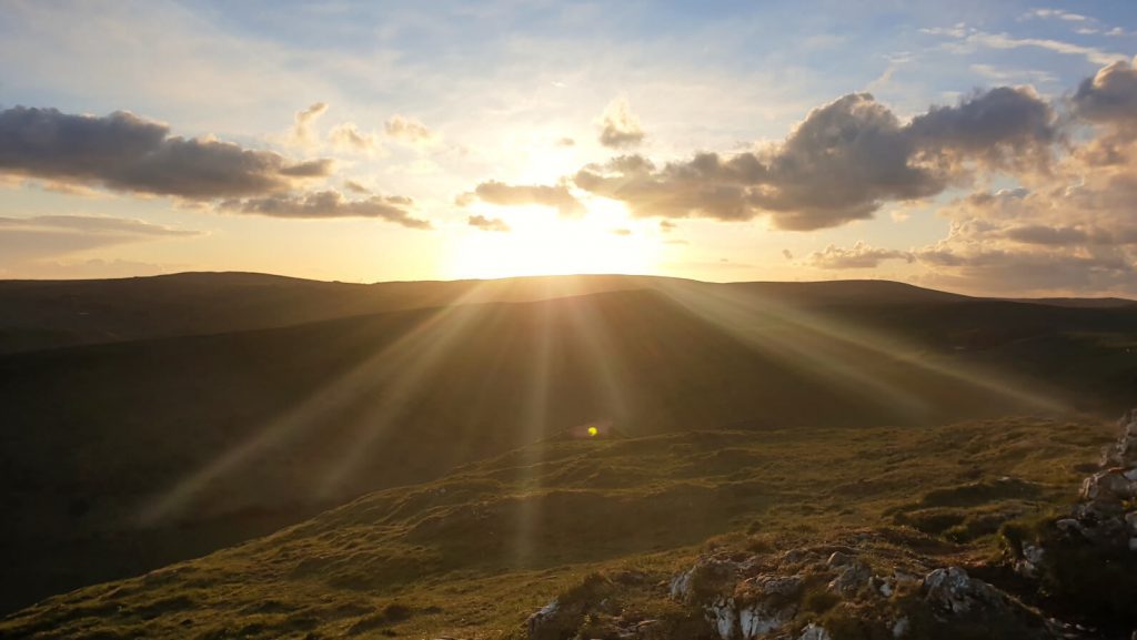 Sunset at the top of Chrome Hill is a true Peak District bucket list item. Pictured are the sun beams bursting through breaks in the clouds over the rolling Peak District hills.