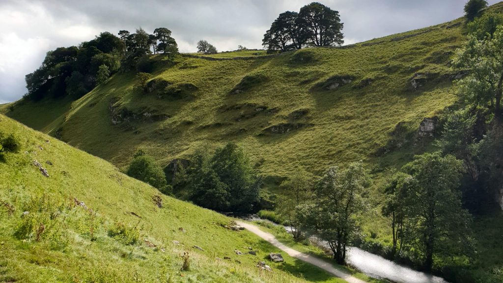 The rugged Wolfscote Dale near Hartington is a stunning place for a walk in the Peak District. The rocky valley walls are covered in grass and trees and dwarf the small path below.