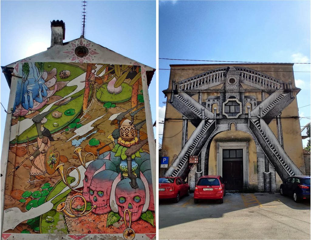 Two sides of buildings are shown both with whole-wall art murals. On the left is a more abstract artwork showing pink and blue skulls playing bugles as a single warrior walks along a path with a bow and arrow. On the right, two black and white staircases have been painted onto the side of the building, slightly obscured by the cars parked outside.