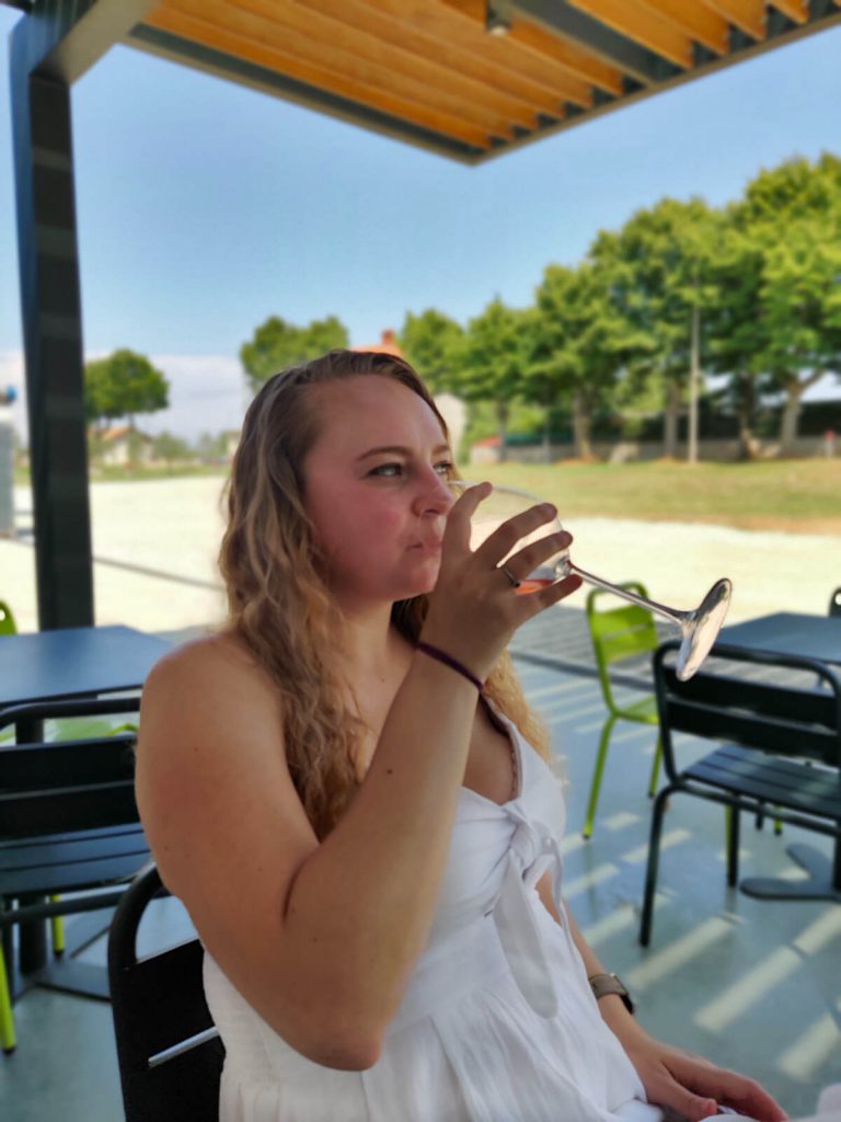 Zoe enjoying her wine tasting experience at Medea Winery, just outside Pula. She is sipping from a glass of rose, with her long blonde hair down and wearing a white dress.
