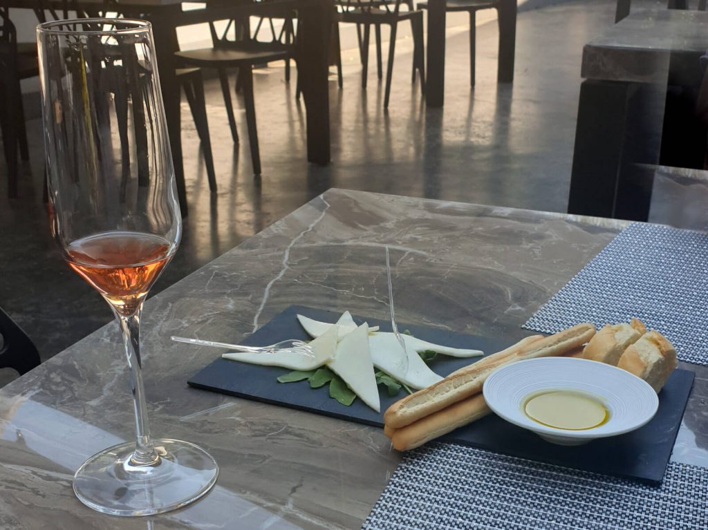 A tasting glass of rose wine with a platter of cheese, breadsticks, sliced french stick and olive oil - the complete Pula wine tasting experience.