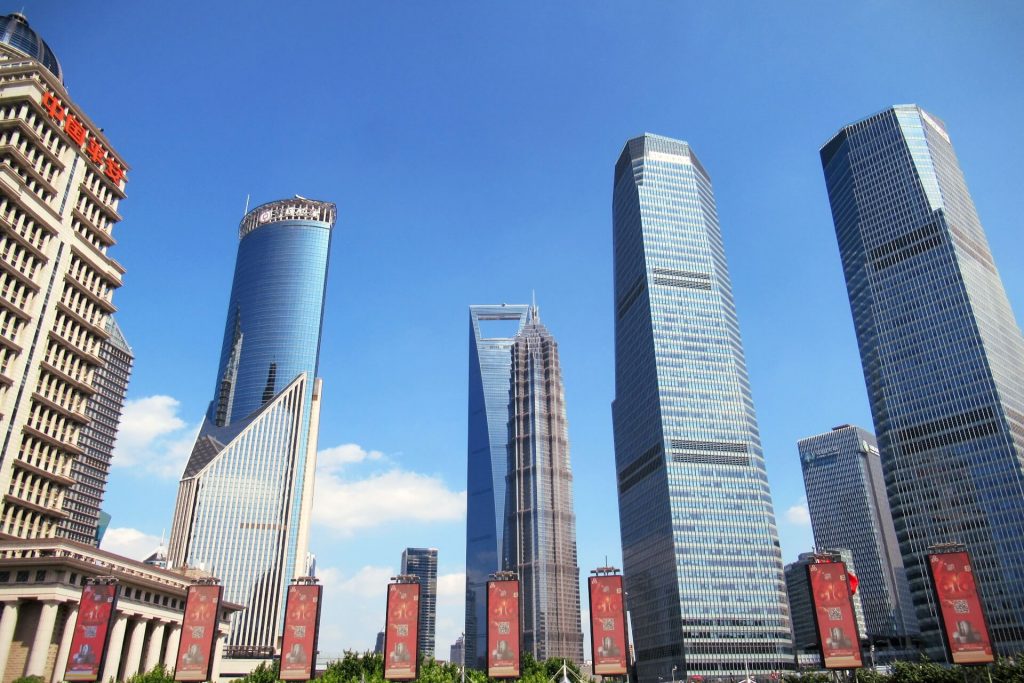 The Shanghai skyline from in front of the Pearl Oriental Tower during a layover with a China Transit Visa, the architecture varies greatly behind the buildings that rise into the crisp blue sky. Visit this during a layover with a China Transit Visa