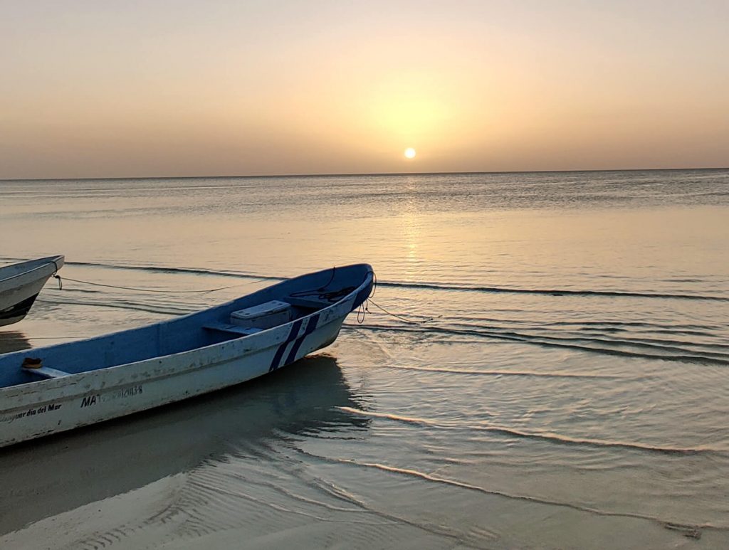 The sun rise over the Caribbean Sea with a small boat in the foreground. Make the journey from Playa del Carmen to Tulum - you won't regret it!