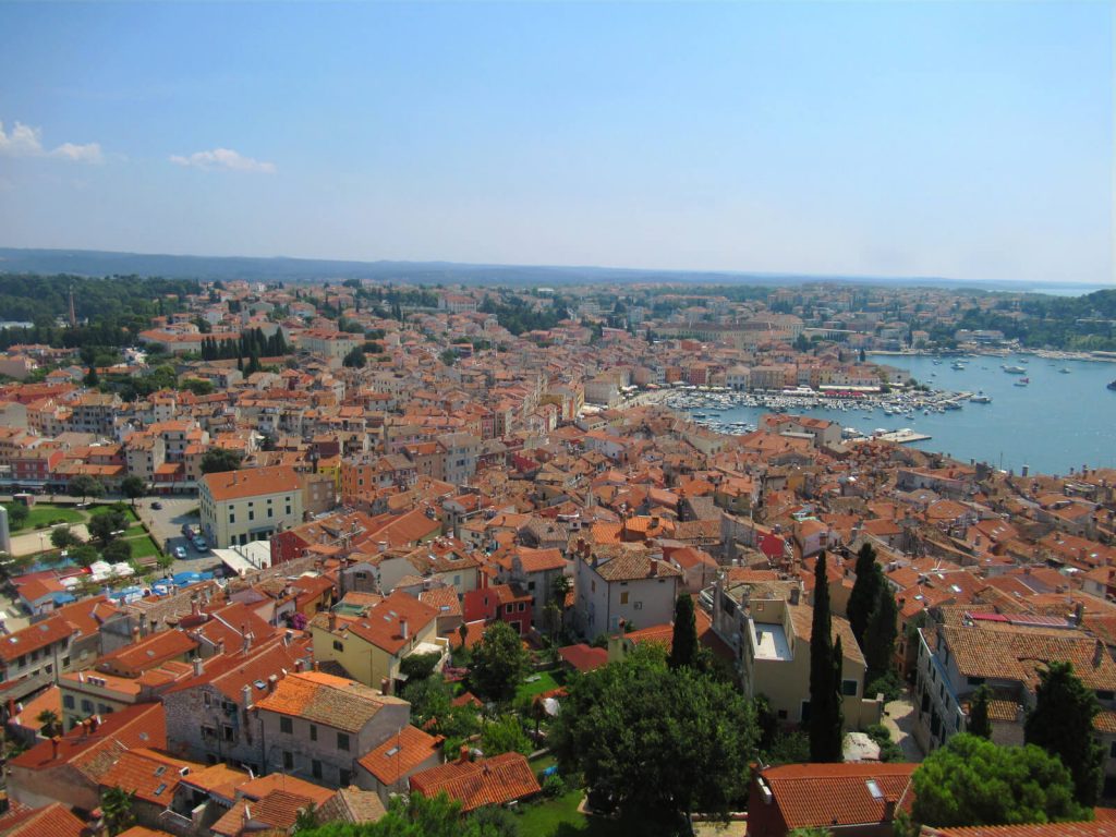 A bird's eye view of Rovinj looking south-east from the bell tower, the best views for your day trip from Pula to Rovinj. Orange roofs, the marina and hills in the distance can all be seen