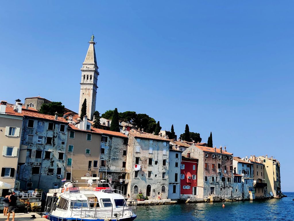 Rovinj looking a lot like Venice with tall buidlings and the sea going right up to the walls of buildings. The bell tower rises up behind the houses on the waters edge.